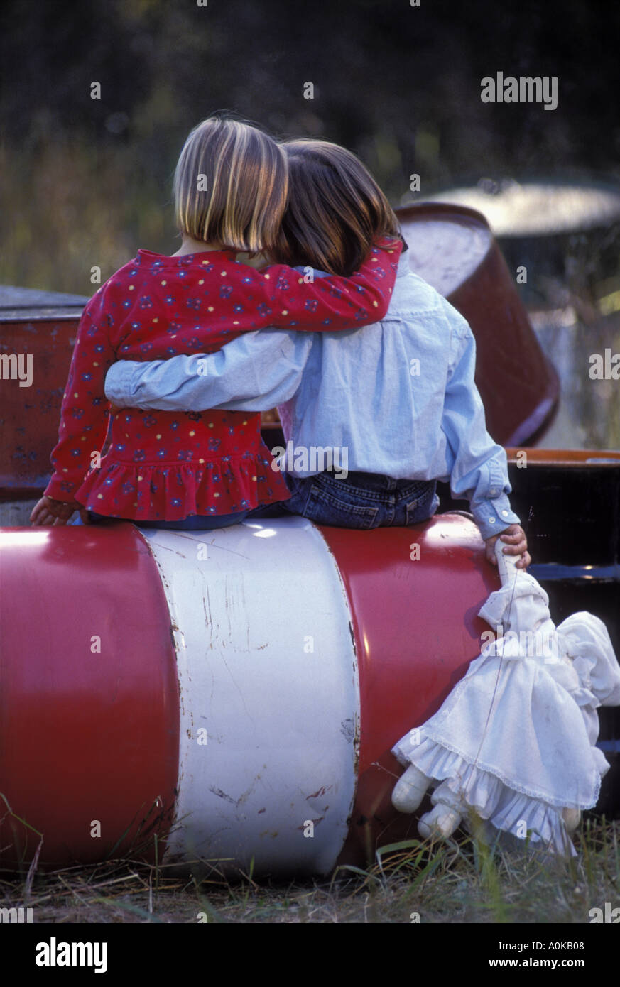 Amici abbracciando mentre è seduto su una vecchia canna chimica illegalmente oggetto di dumping in un campo Foto Stock
