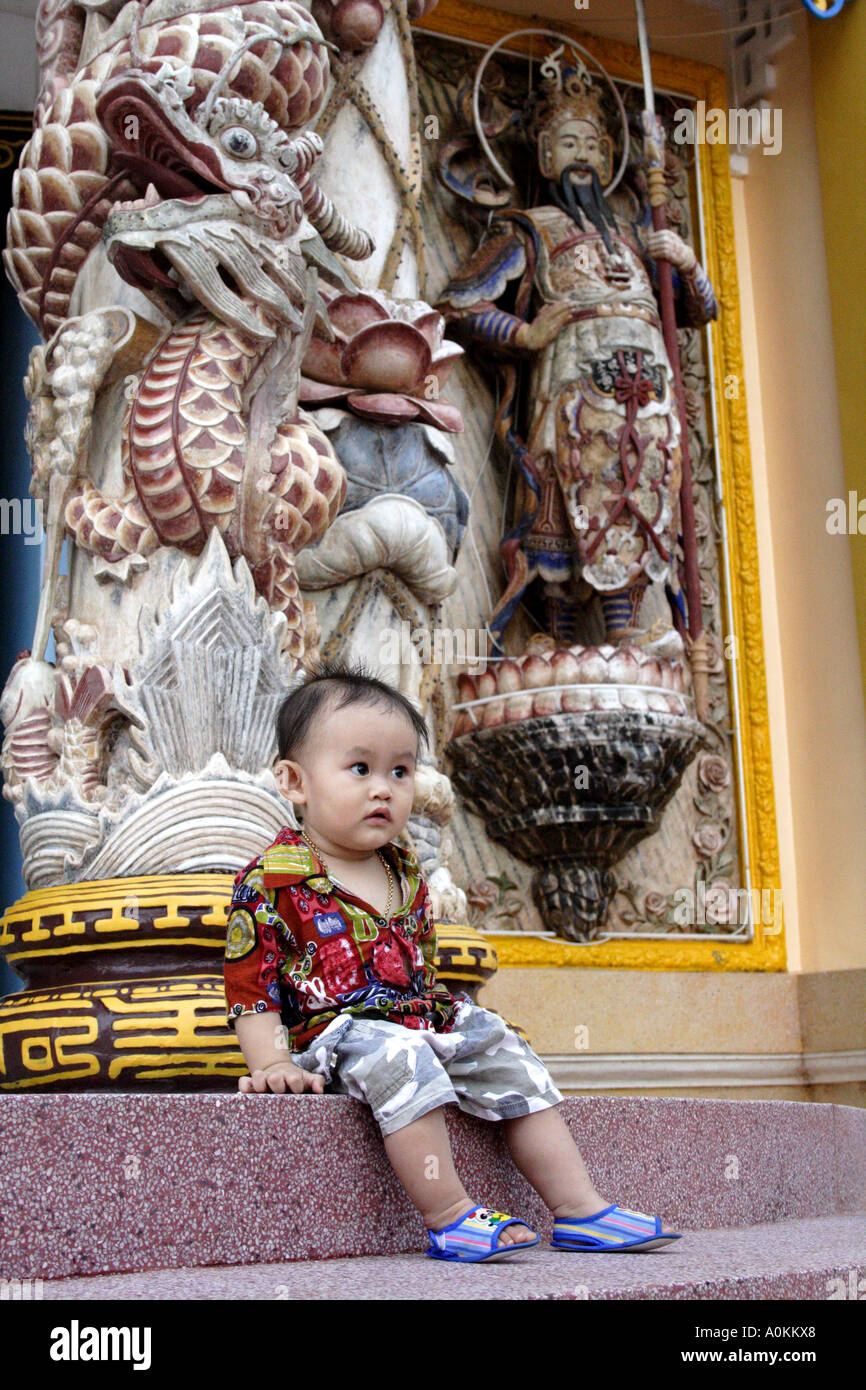 Piccolo Ragazzo seduto su un gradino in corrispondenza di Cao Dai temple (il grande tempio, la Santa Sede) a Tay Ninh, Vietnam Foto Stock
