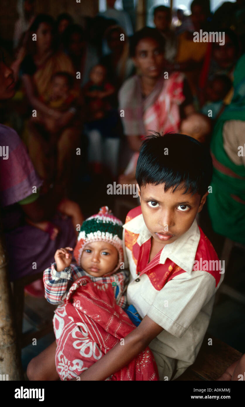 Un ragazzo tiene il suo bambino la sorella a un bambino centro di immunizzazione a Dacca in Bangladesh Foto Stock