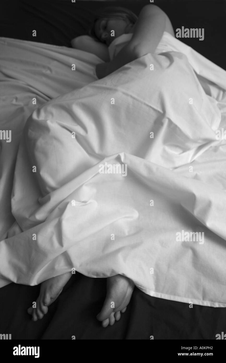 Un solitario femmina bianco giacente in letto sotto un foglio bianco contro un coperchio scuro. Foto Stock