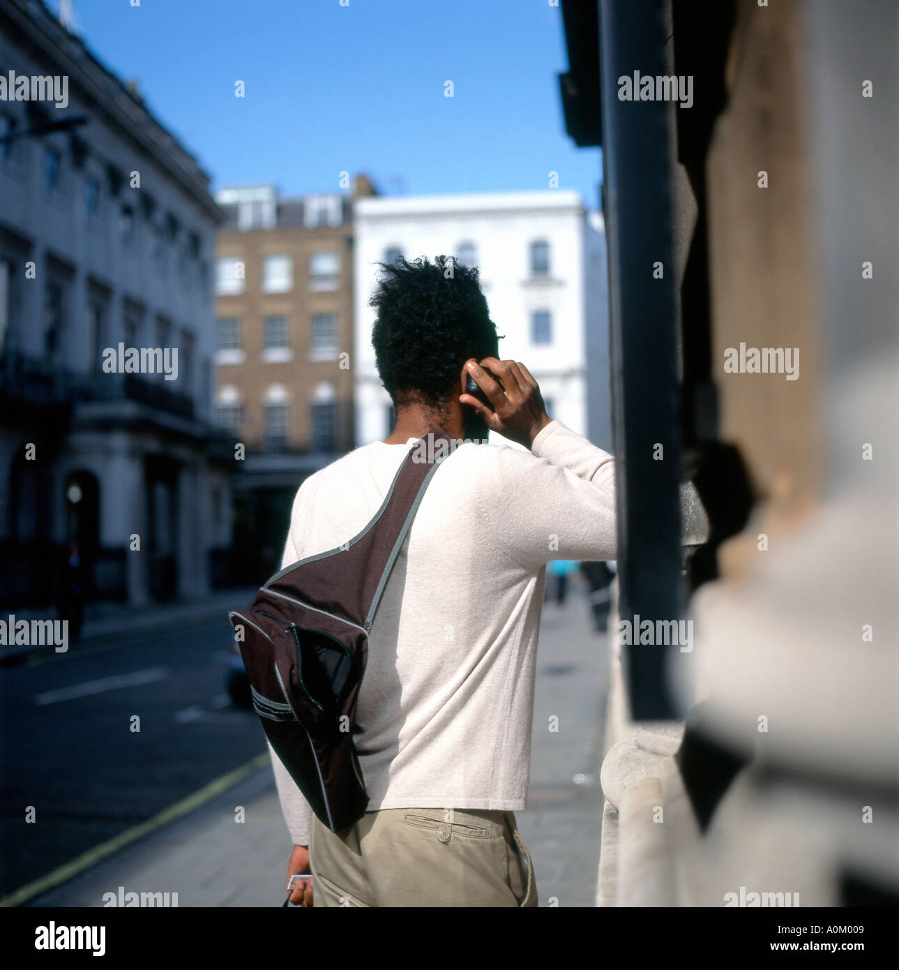 Vista posteriore di un uomo nero alla moda con spalla zaino in borsa utilizzando un vecchio telefono cellulare in un via a Londra Inghilterra Regno Unito 2004 KATHY DEWITT Foto Stock