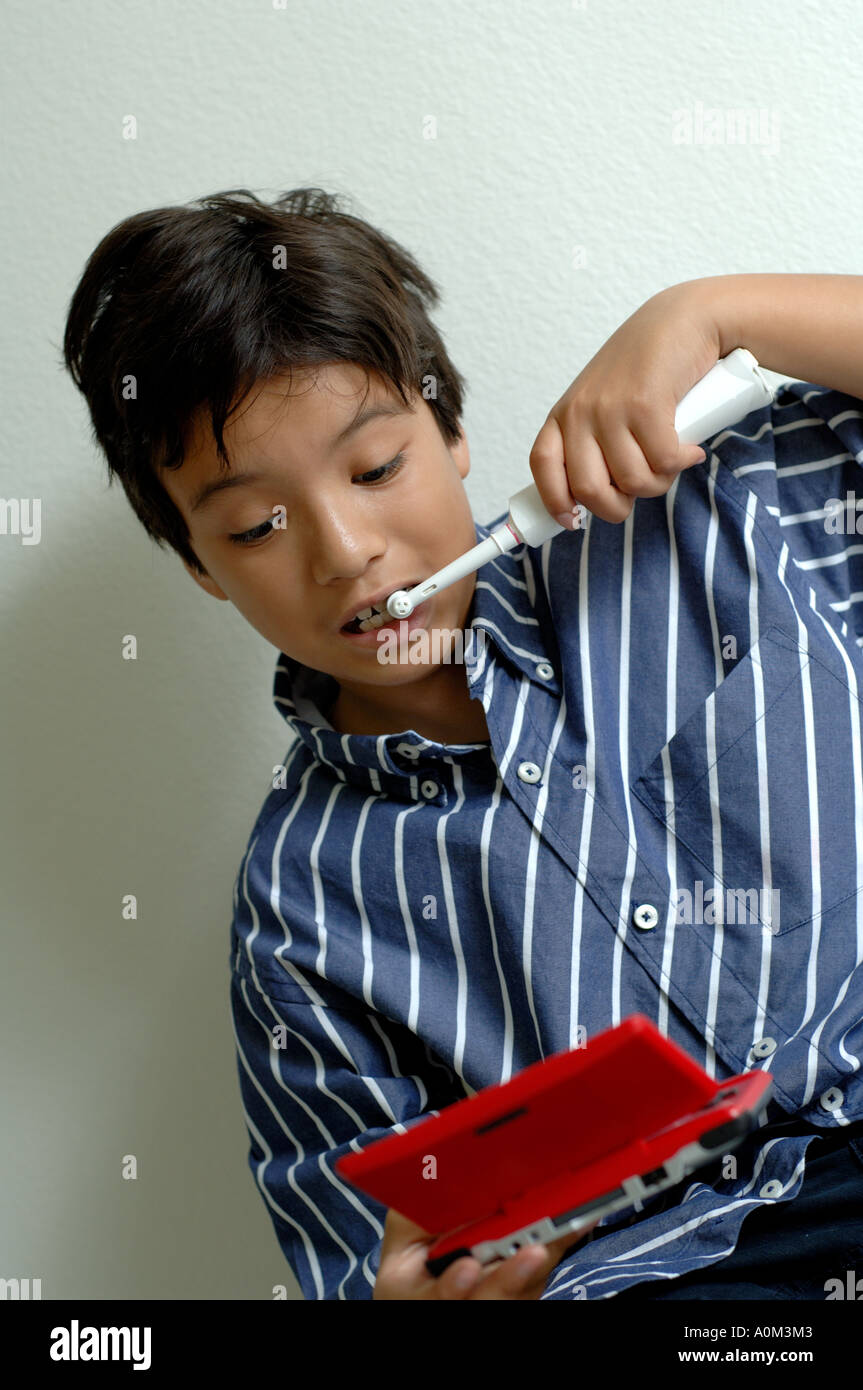 Ragazzo giovane spazzolatura dei denti e riproduzione portatile palmare video gioco Foto Stock