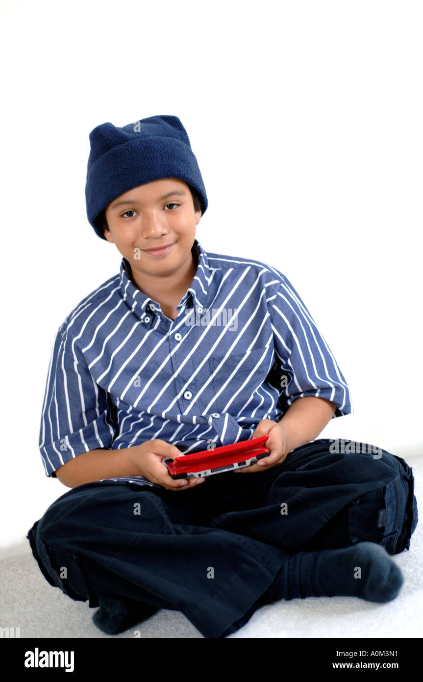 Ritratto di 9 anni vecchio ragazzo seduto sul pavimento con le gambe incrociate a giocare con un palmare video gioco Foto Stock
