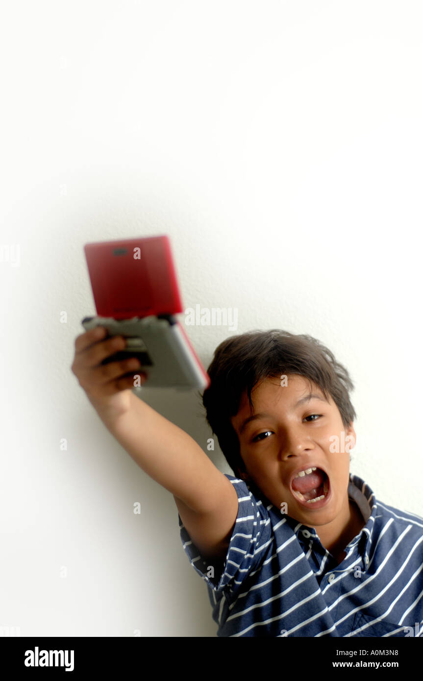 Ritratto di 9 anni vecchio ragazzo giocando con un palmare video gioco, tenendo in aria. Ho vinto l'espressione. Foto Stock