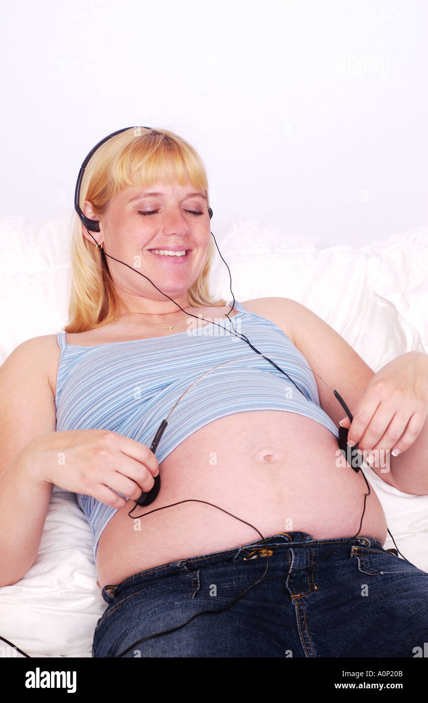 Donna incinta rilassante letto in ascolto di musica e la partecipazione delle cuffie sulla pancia Foto Stock
