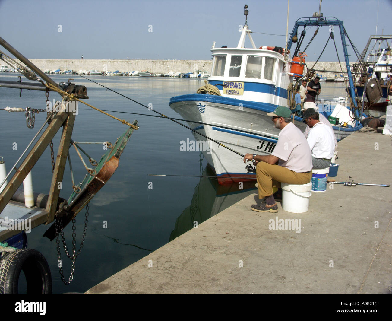 Tre pescatori pesca con asta e riga accanto ad una pesca commerciale barca, Puerto Deportivo de Fuengirola, Fuengirola, Spagna Foto Stock