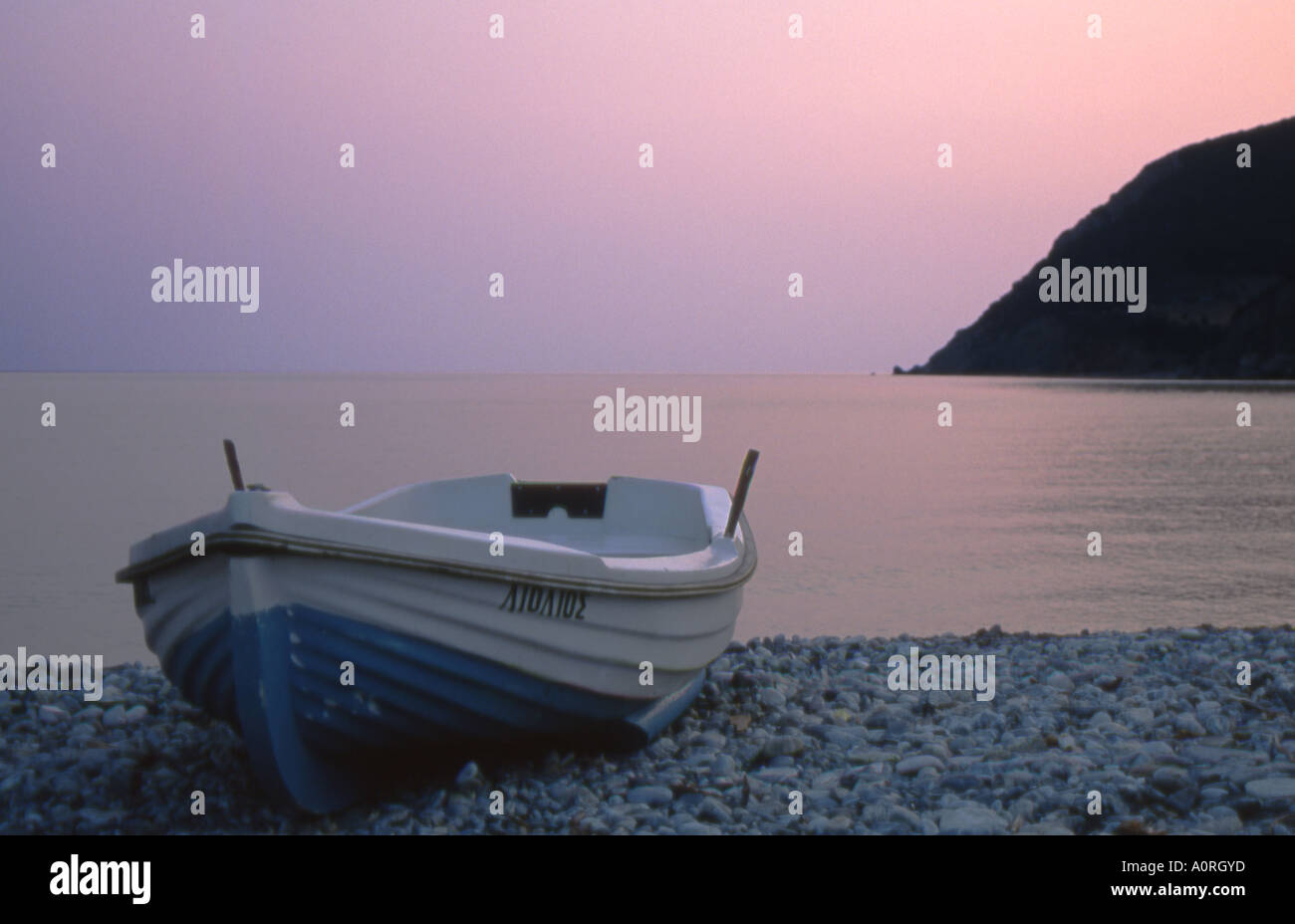 Lone barca da pesca spiaggiata su ciottoli in rosa alba sky n1658 Foto Stock