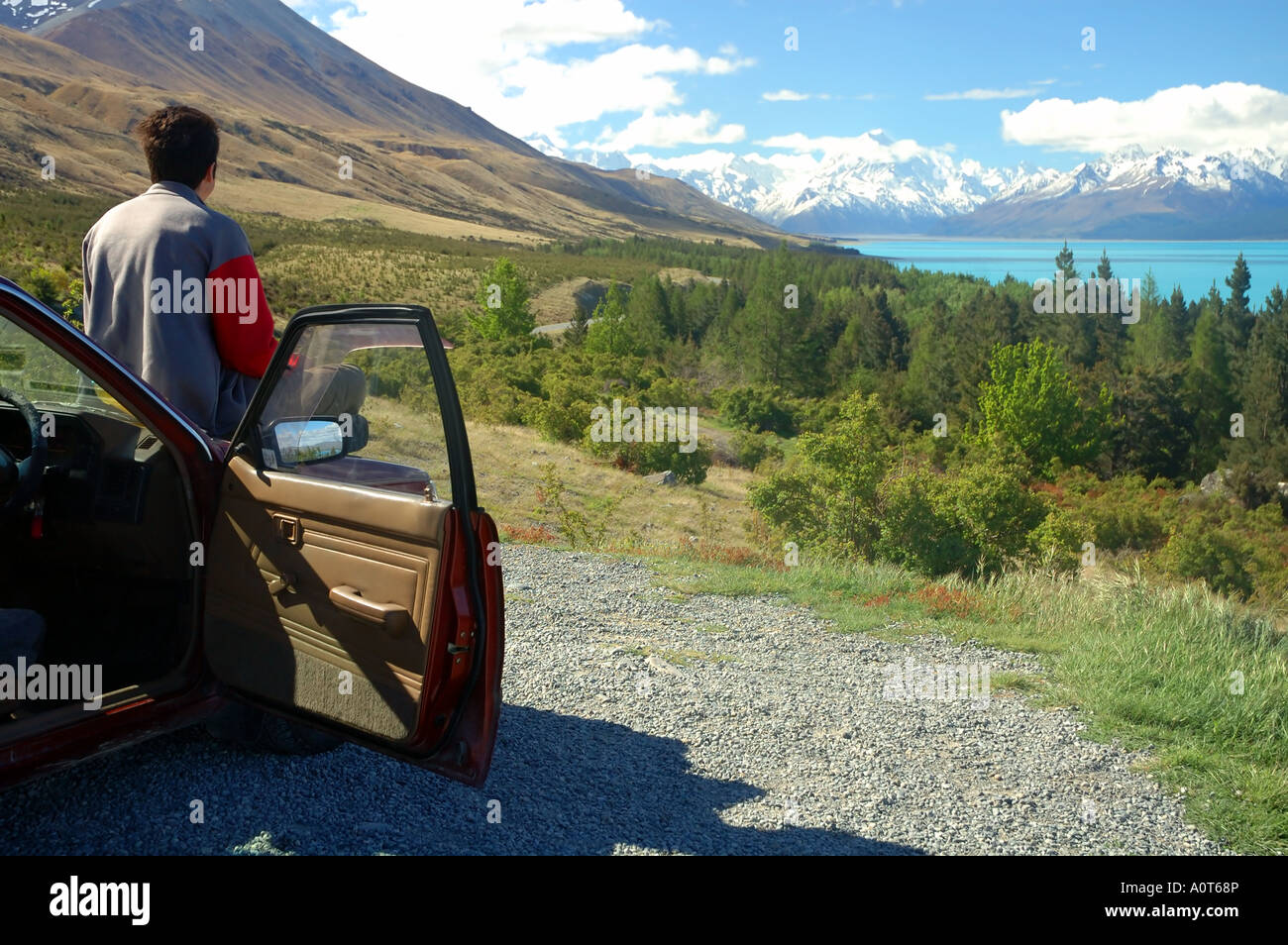 Viaggiatore sul cofano auto contemplando il vertice di Aoraki Mt Cook attraverso il Lago Pukaki, Nuova Zelanda Foto Stock