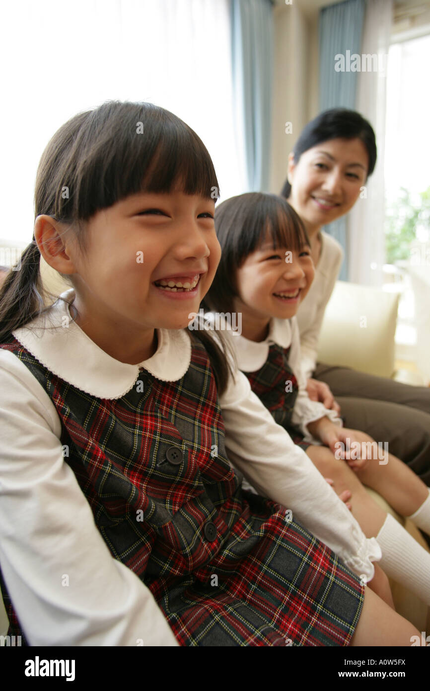 Due ragazze e la loro madre seduta su un divano e sorridente Foto Stock