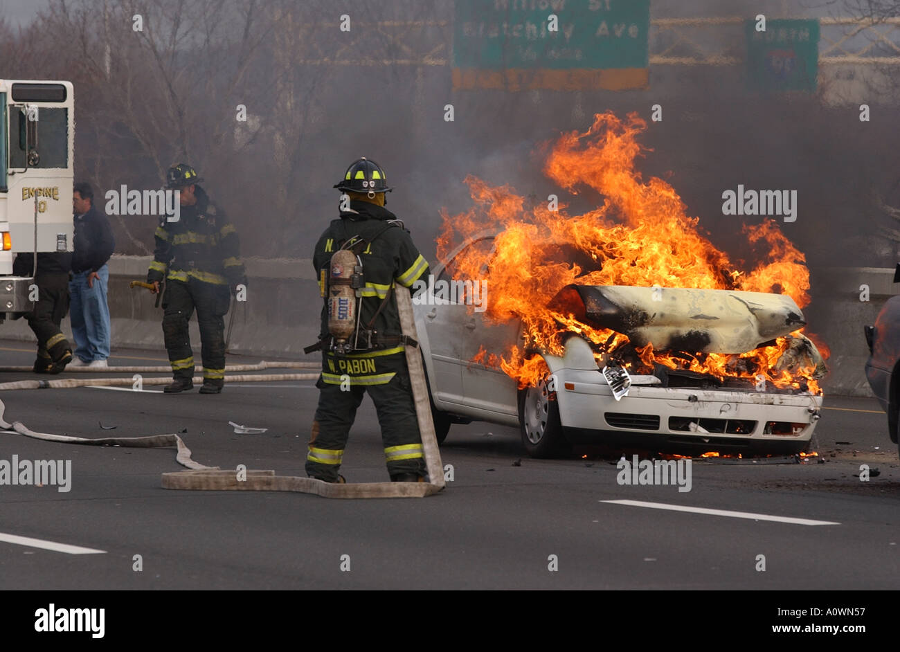 Un vigile del fuoco combattono una macchina fuoco attende per acqua come egli detiene un tubo flessibile Foto Stock