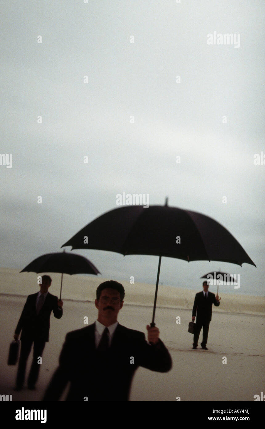Silhouette di tre uomini di affari ombrelli azienda in un deserto Foto Stock