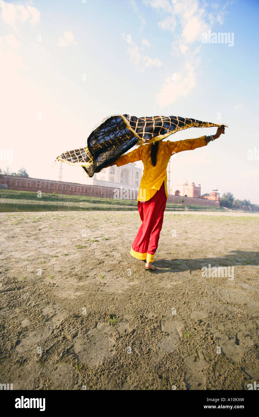 Vista posteriore di una giovane donna che mantiene la sua stola sulla riva del fiume, Taj Mahal, Agra, Uttar Pradesh, India Foto Stock