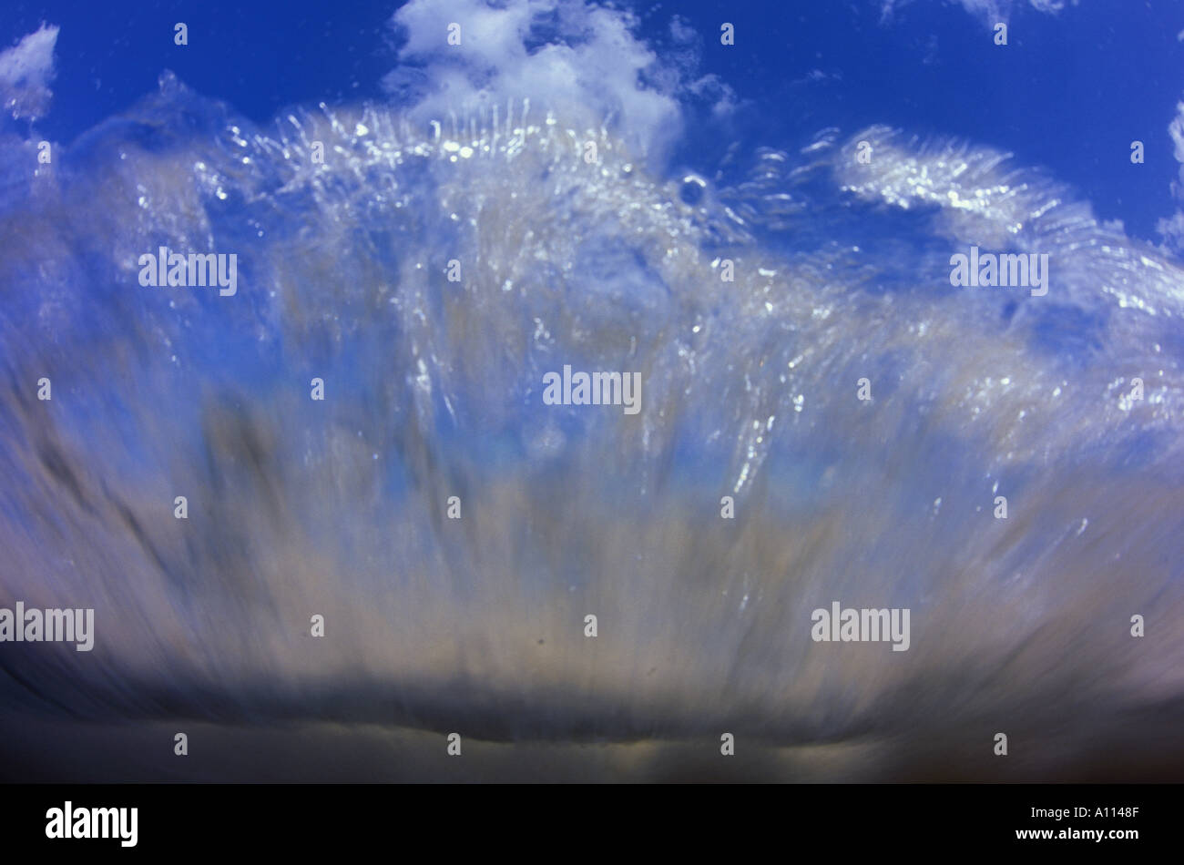 Un'onda schizza sopra la parte anteriore della lente della fotocamera portando bolle e sabbia con esso mentre ancora mostra una vista del cielo Foto Stock