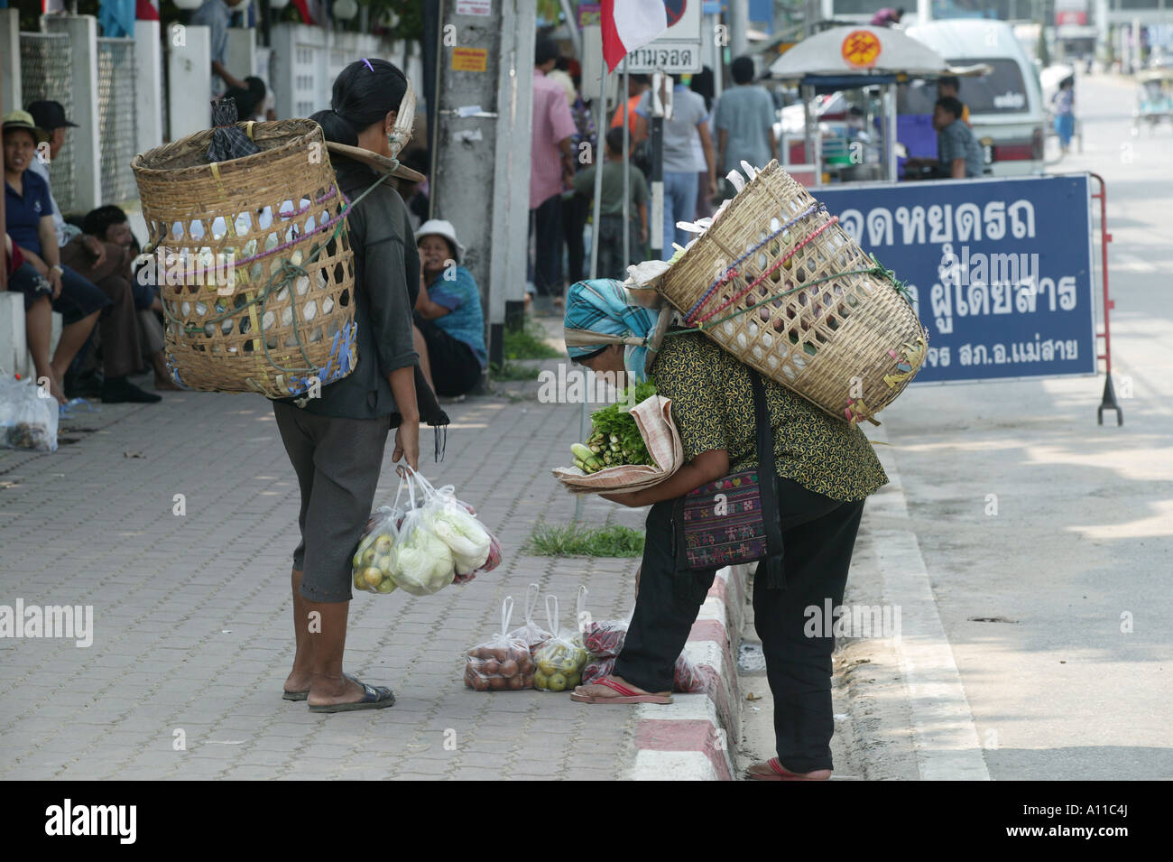 Due donne della tribù della collina di commercianti che trasportano grandi cesto pieno di frutta e verdura sulle loro spalle circa per vendere la loro mercanzia in strada Mai Sai Foto Stock