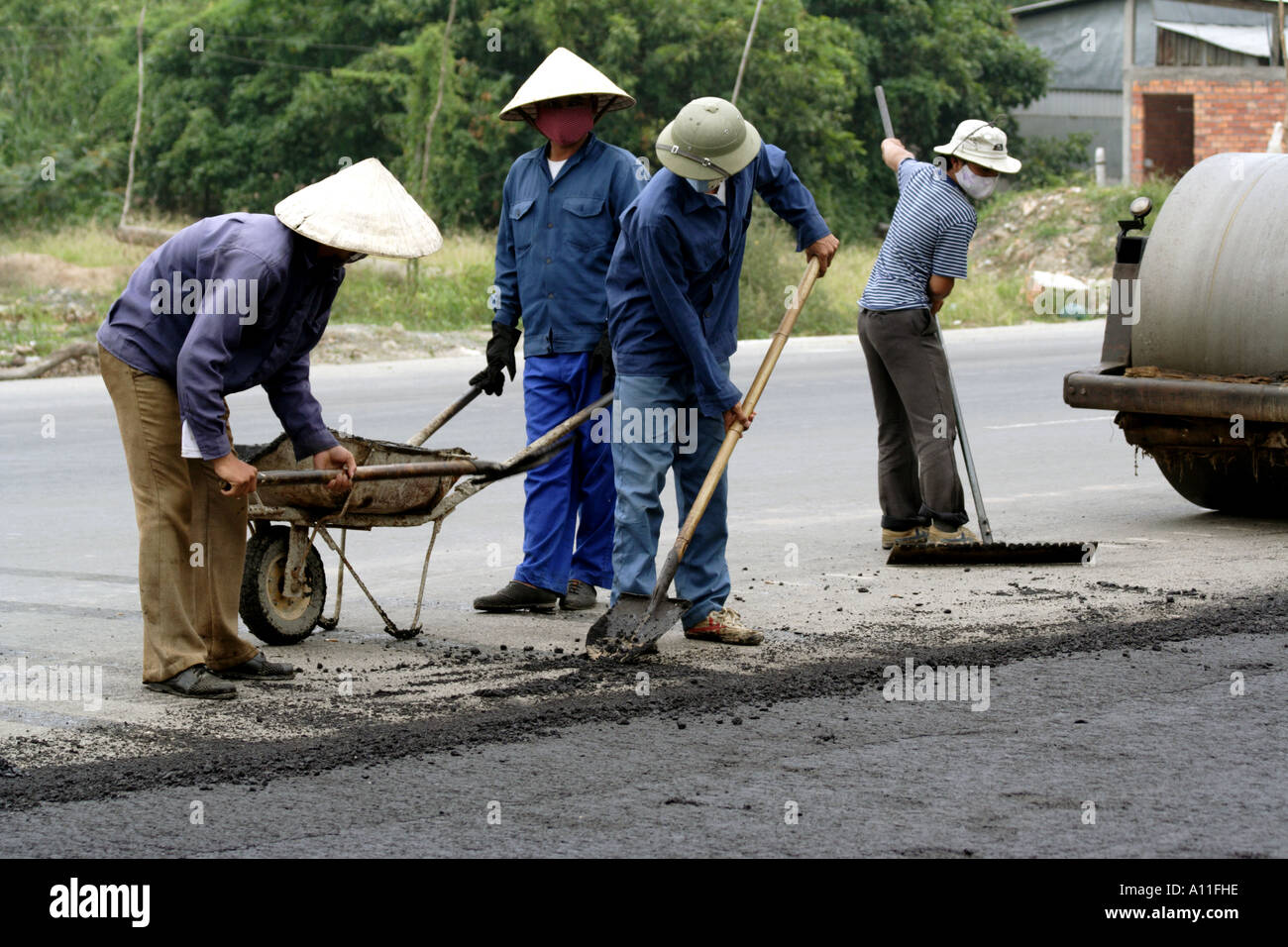 Operai pala in anticipo del rullo compressore durante la costruzione della strada di Saigon (HCMC) al Delta del Mekong, Vietnam Foto Stock