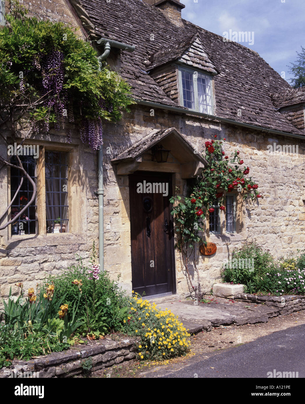 Le rose e i fiori intorno alla porta di Cotswold Cottage nel villaggio di Little Barrington Foto Stock