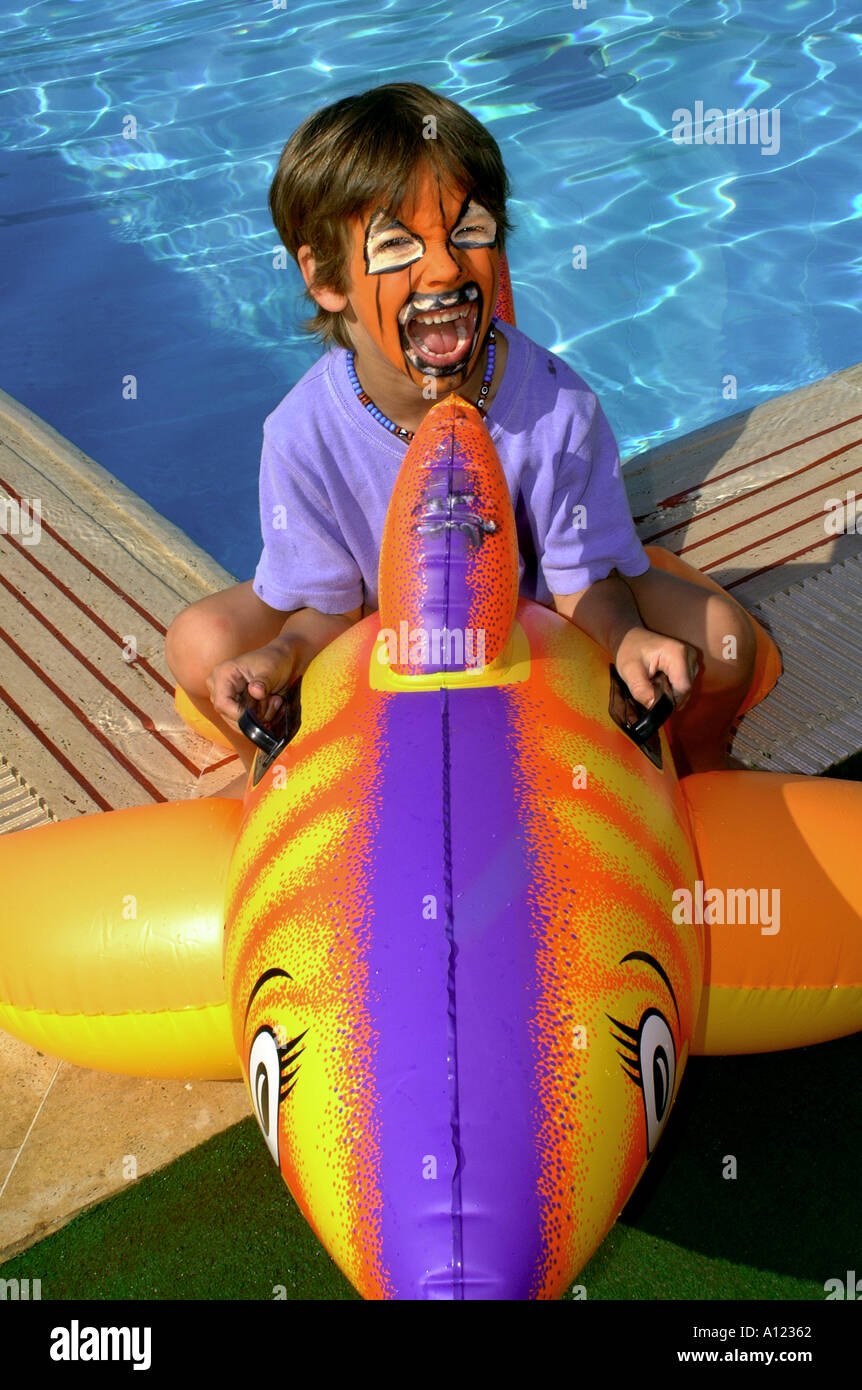 Ragazzo seduto su Blow up shark in piscina Foto Stock