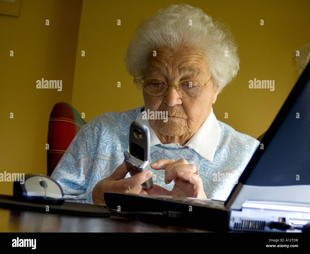 ANZIANI TELEFONO CELLULARE COMPOSIZIONE anziani 80-90 anni Pensivo signora on chiamare o inviare messaggi di testo con il telefono cellulare mentre si è seduti sul computer portatile Foto Stock