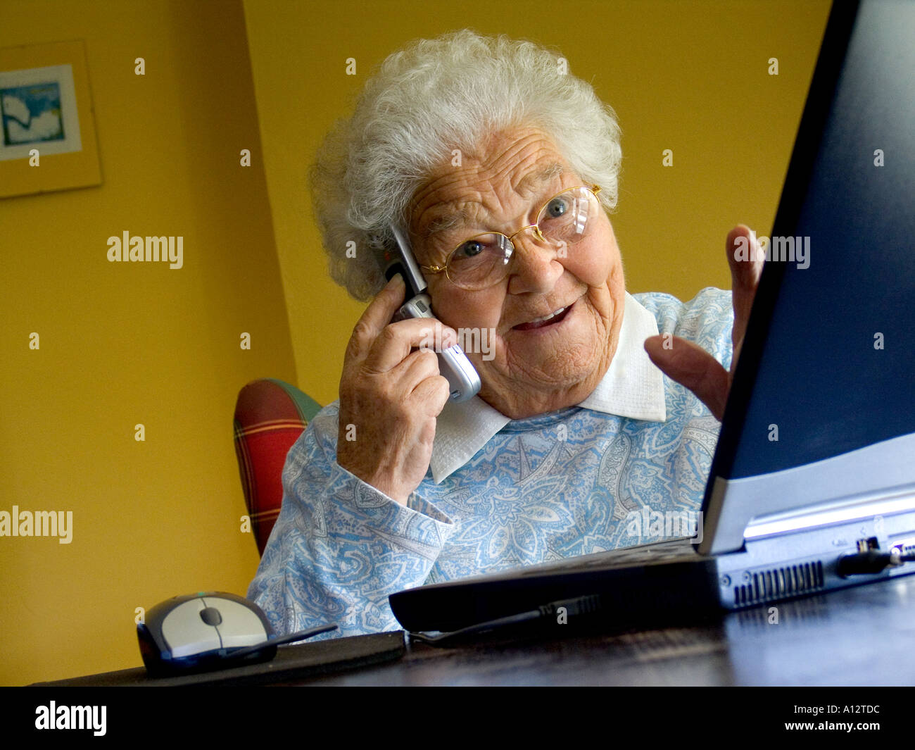 Anziana donna anziana e vivace al computer è affascinata e stupita dalla sua nuova tecnologia per lo schermo del computer portatile e che parla al suo telefono cellulare Foto Stock