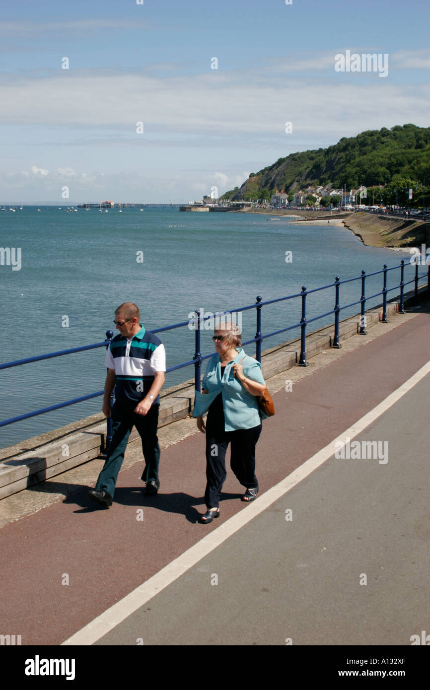 I turisti passeggiando lungo la promenade con MUMBLES PIER IN BACKGROUND, Swansea, West Glamorgan, South wales, Regno Unito Foto Stock