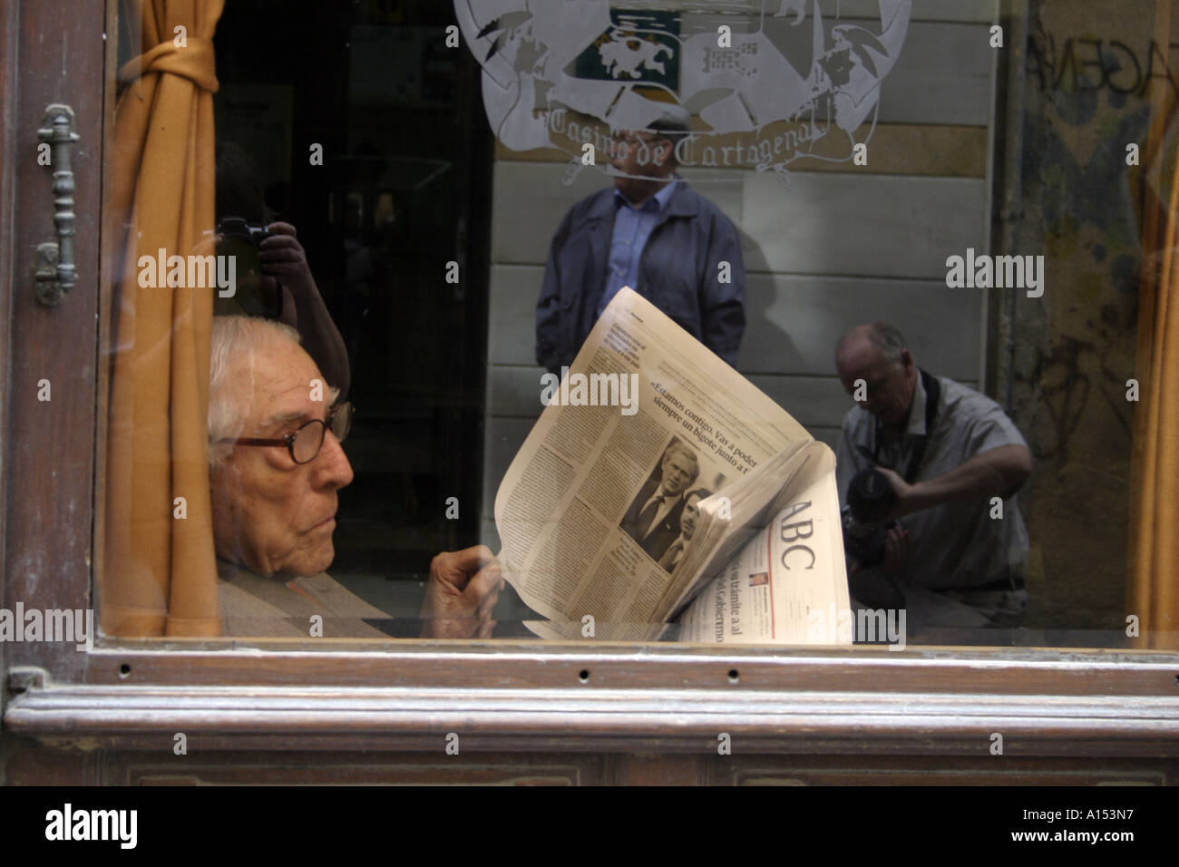 Anziano Signore leggere giornale e guardando fuori sulla vita di strada In un caffè spagnolo Foto Stock