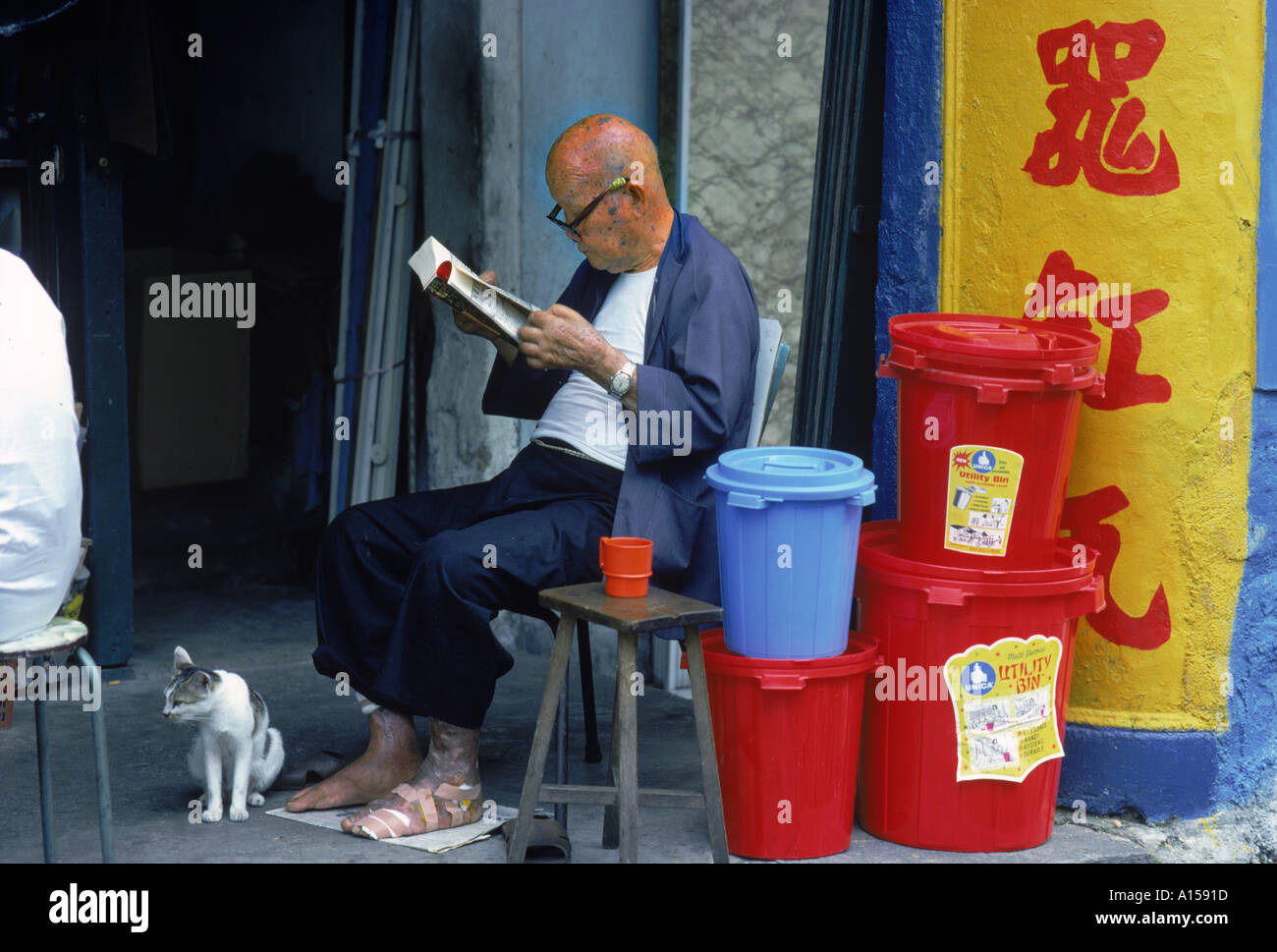 Ritratto di un uomo anziano con piede bendato indossa occhiali e la lettura di un libro seduti con il suo gatto accanto a un mucchio di Foto Stock