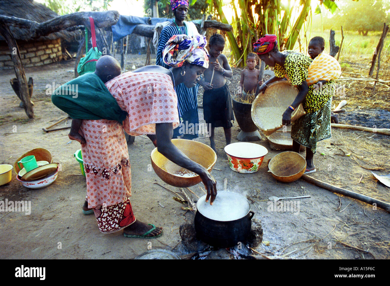 Le donne gli abitanti di un villaggio da Fulani villaggio di Dembel Jumpora preparare il riso per la cena con i loro bimbi allacciati ai loro Foto Stock