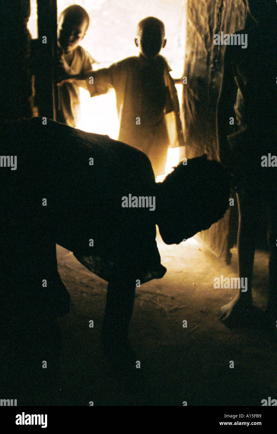 Lama Uma spazza la sua capanna mentre i figli si guarda nel villaggio di Dembel Jumpora nel paese africano e Dell'ovest della Guinea Foto Stock