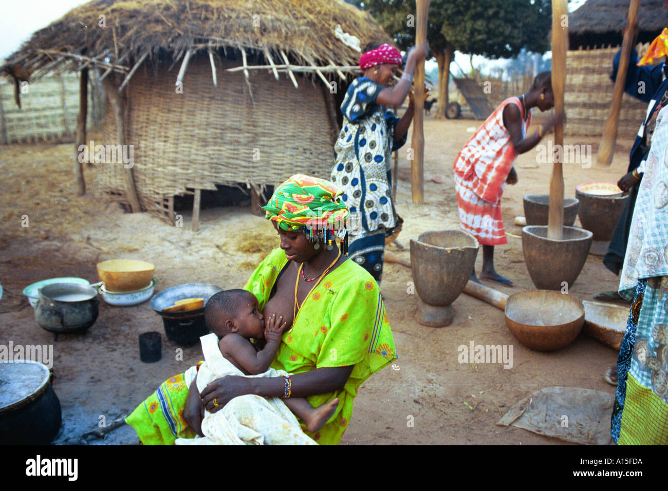 Una madre nutre il suo bambino che nasce come altre donne libbra di riso in preparazione per la cena in Fulani villaggio di Dembel Jumpora Foto Stock