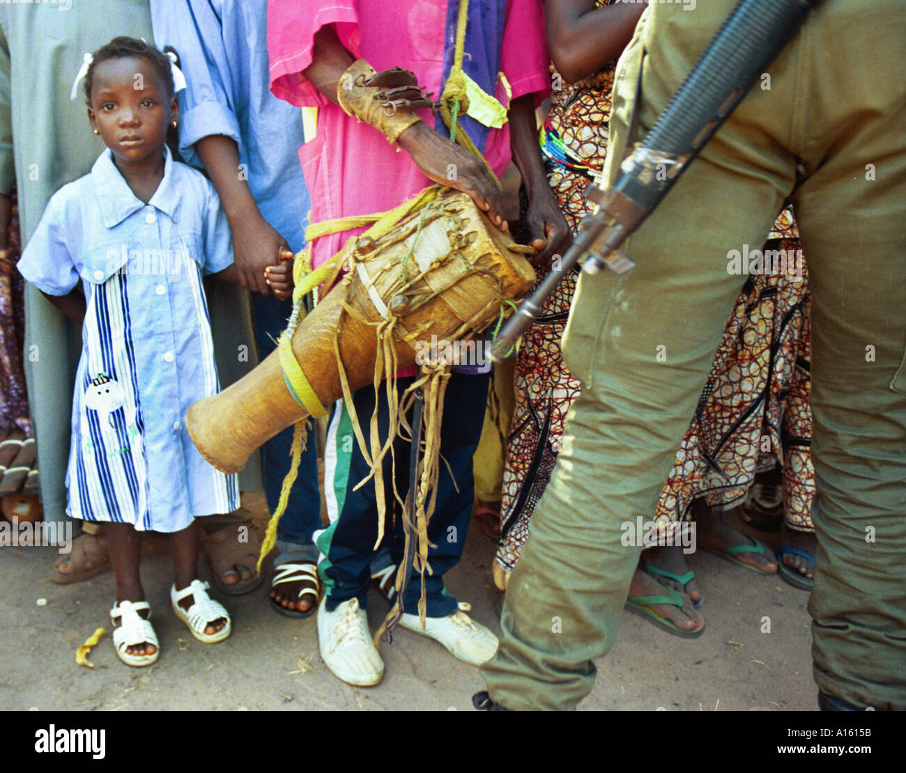 Un Occidente ragazza africana detiene sul suo madri mano come un soldato senegalese spinge indietro una folla durante un festival per la pace in Foto Stock