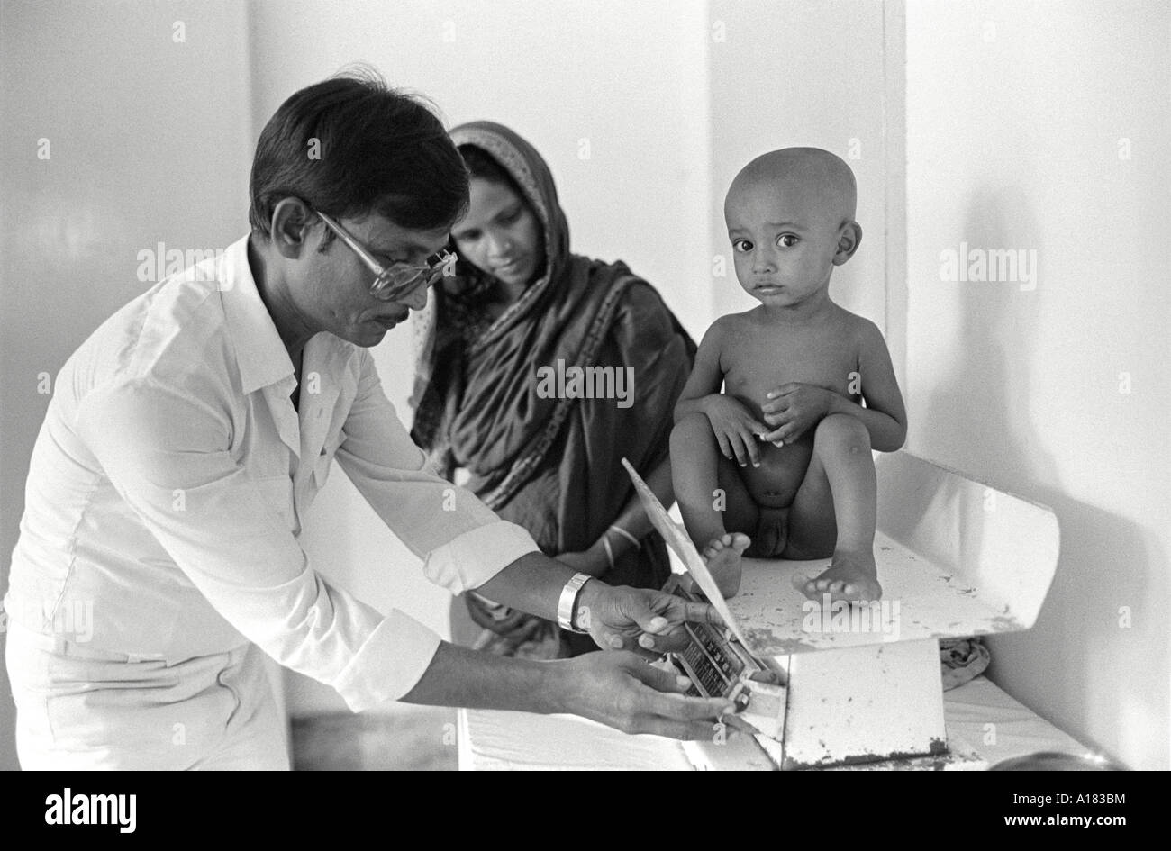 B/N di un medico che pesa un bambino malnutrito nella Children's Nutrition Unit, Dhaka, Bangladesh Foto Stock