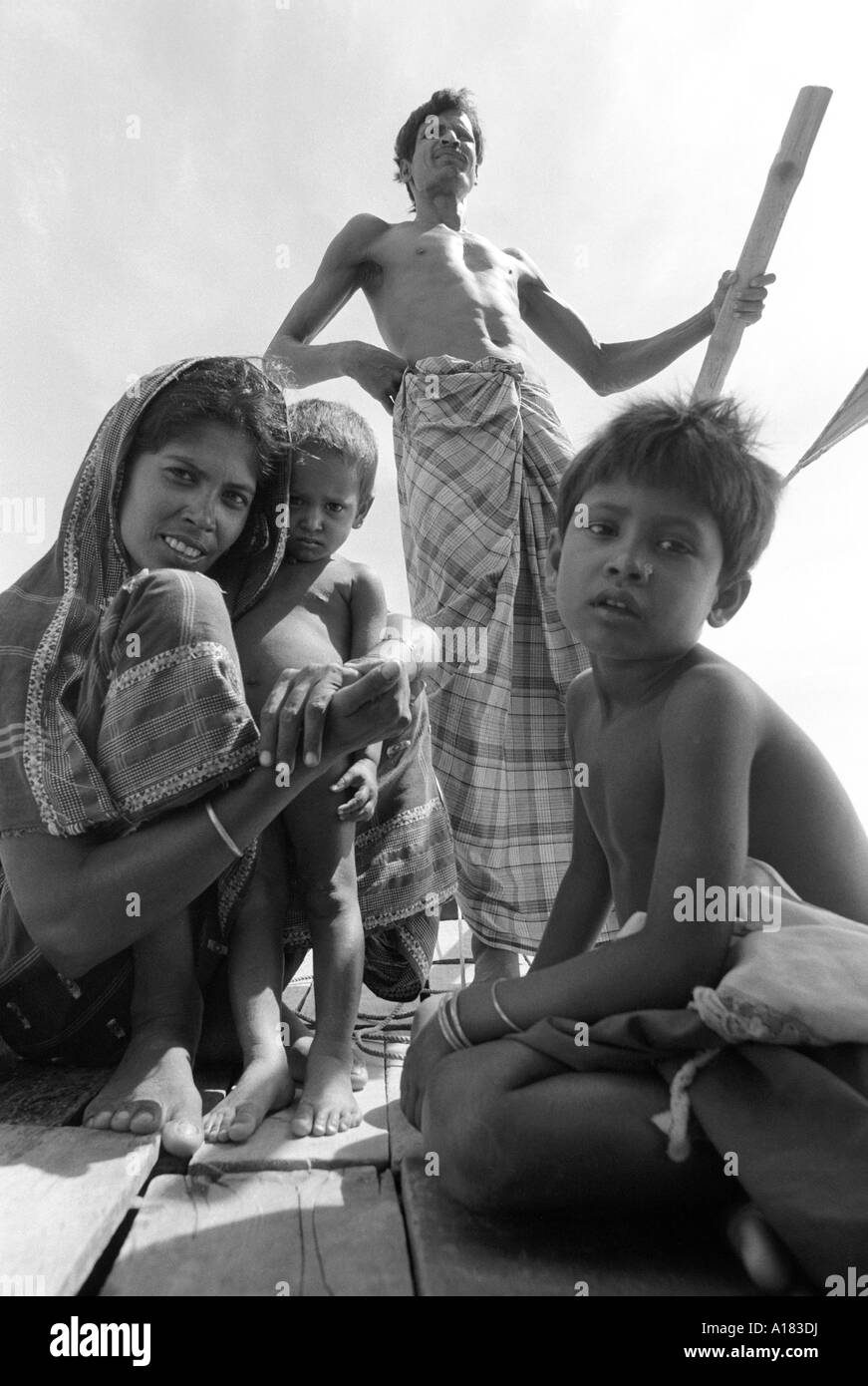 B/N di una donna e due bambini su un piccolo traghetto fluviale con il ferrista che guida sul retro della barca su un affluente del Gange, Bangladesh Foto Stock