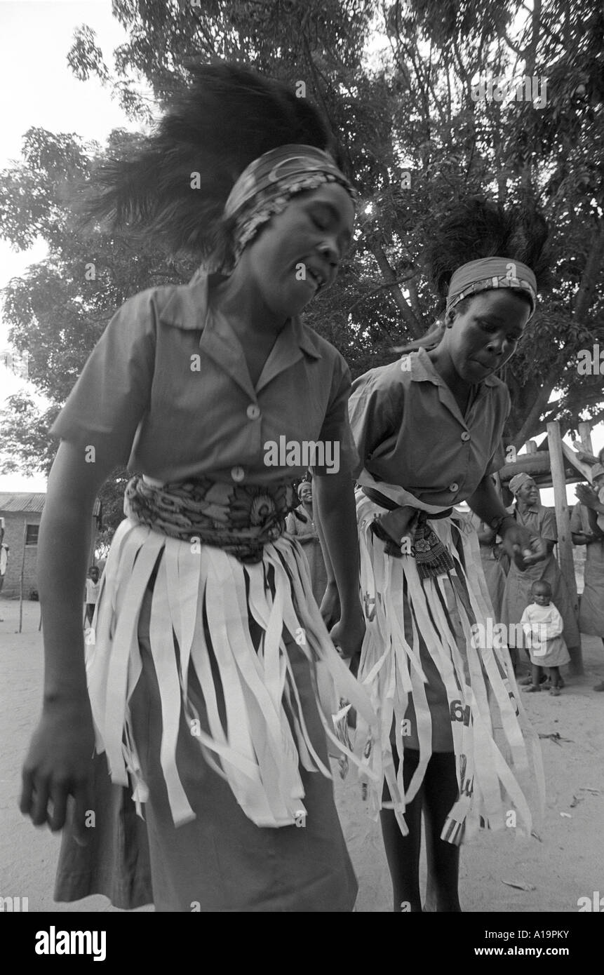 B/N di due lavoratrici agricole Batonga in moderno e parziale abito cerimoniale tradizionale che esegue una danza di benvenuto. Centenario, Zimbabwe Foto Stock