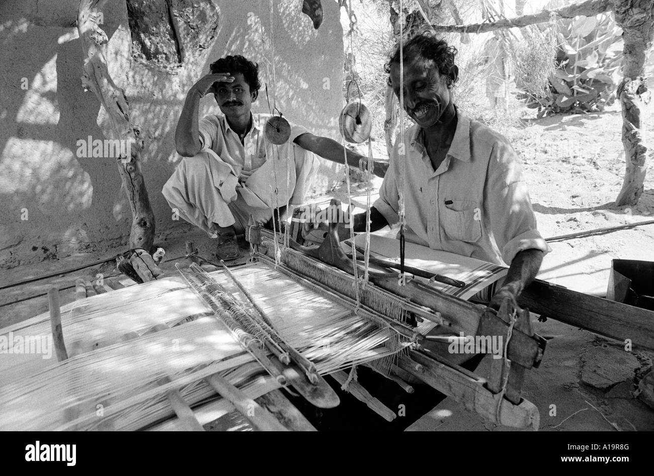 B/N di un tessitore sorridente che lavora ad un telaio di buca tradizionale. Islamkot, regione di Tharparkar, Pakistan Foto Stock