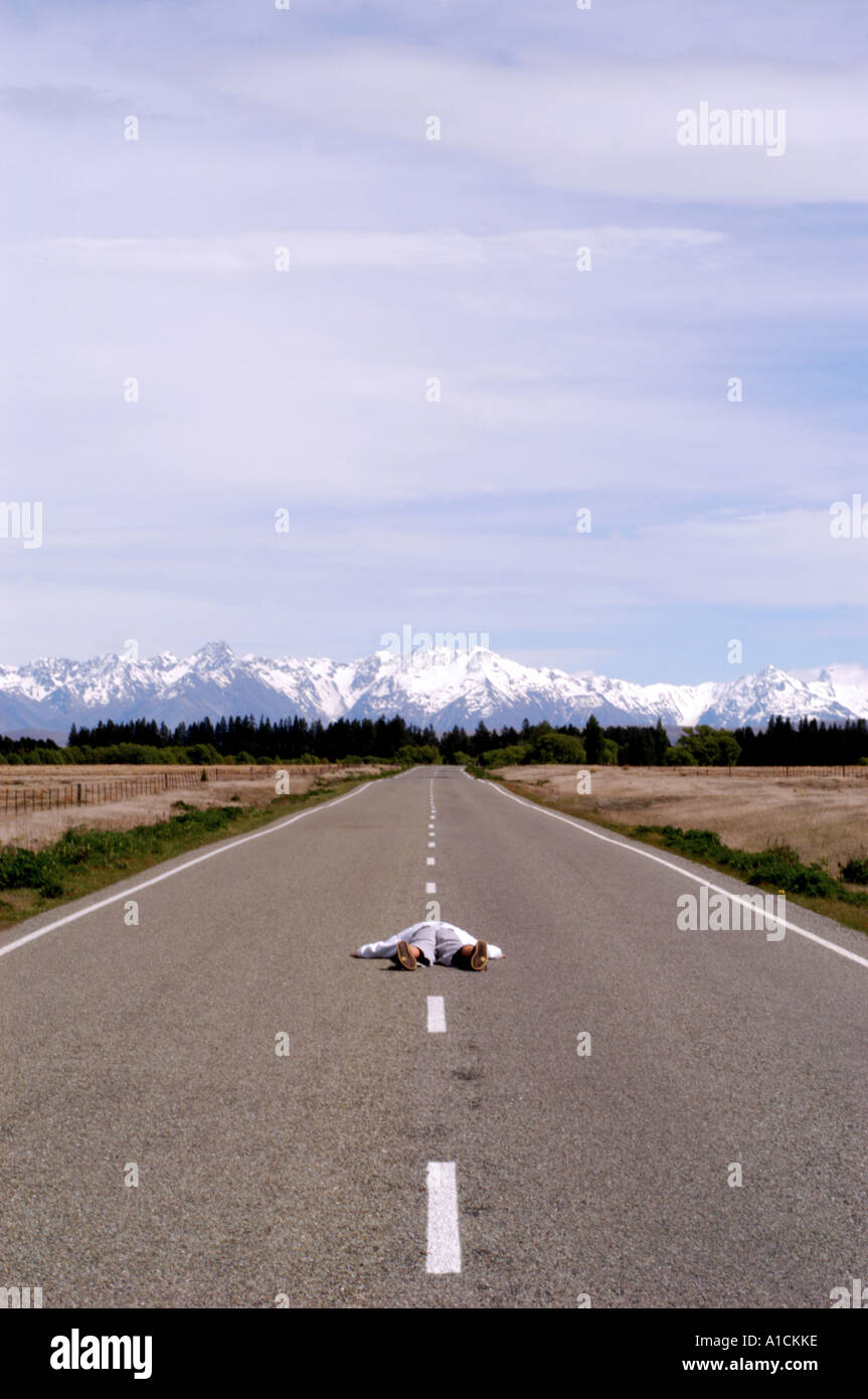 L'Uomo sdraiato in strada dopo una camminata lunga e lunga la strada da percorrere Foto Stock