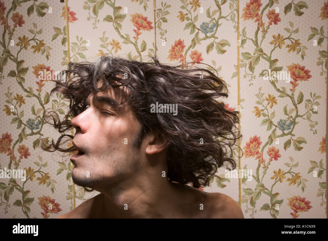 Profilo laterale di un uomo con lunghi capelli ricci contro la carta da parati floreale che scuote la testa Foto Stock