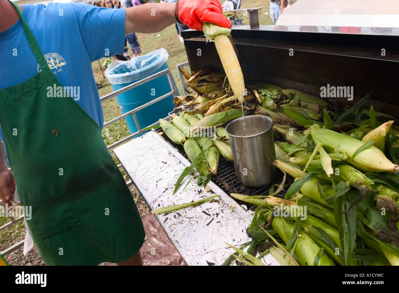Fornitore maschio ad una fiera in Connecticut USA immergendo una spiga di grano in un contenitore di burro fuso che è accanto a un mucchio di roa Foto Stock