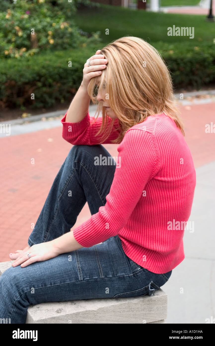 Giovane donna bionda che con il suo profilo per la telecamera seduta su un mattone e cemento pilastro Modello rilasciato Foto Stock