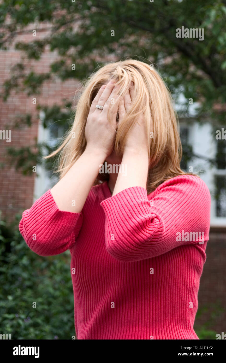 Giovane donna bionda che coprono la maggior parte del suo viso con le sue mani modello rilasciato Foto Stock