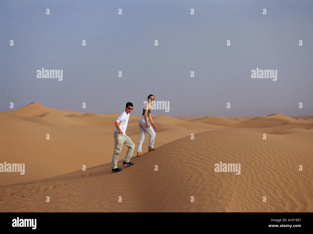 Giovane uomo e donna a piedi fino le dune di sabbia del deserto del Sahara in Marocco Foto Stock