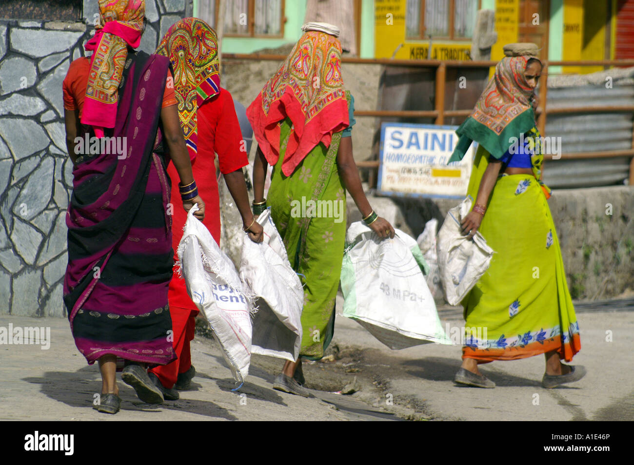 Team quattro donne indiane in sari colorati lavorando duro che trasportano svuotare i sacchi di sabbia a street sito in costruzione, India Foto Stock