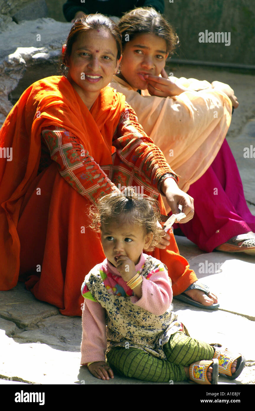 Due generazioni della famiglia indiana in abito tradizionale seduta di fronte a casa in legno, Manikaran, India Foto Stock