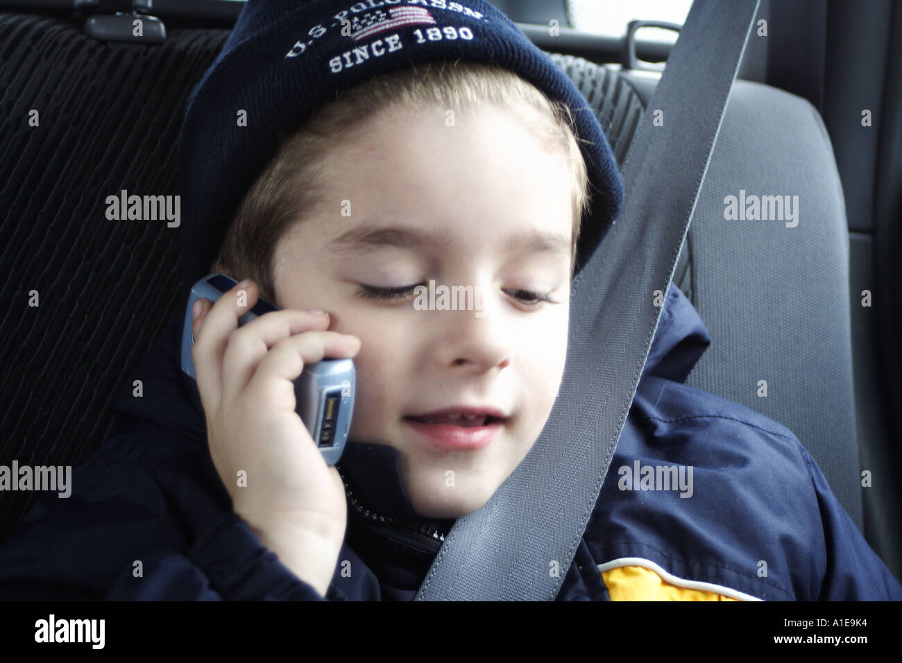 Poco boy parlando al telefono con la sua mamy. In auto. La cintura di sicurezza. Foto Stock