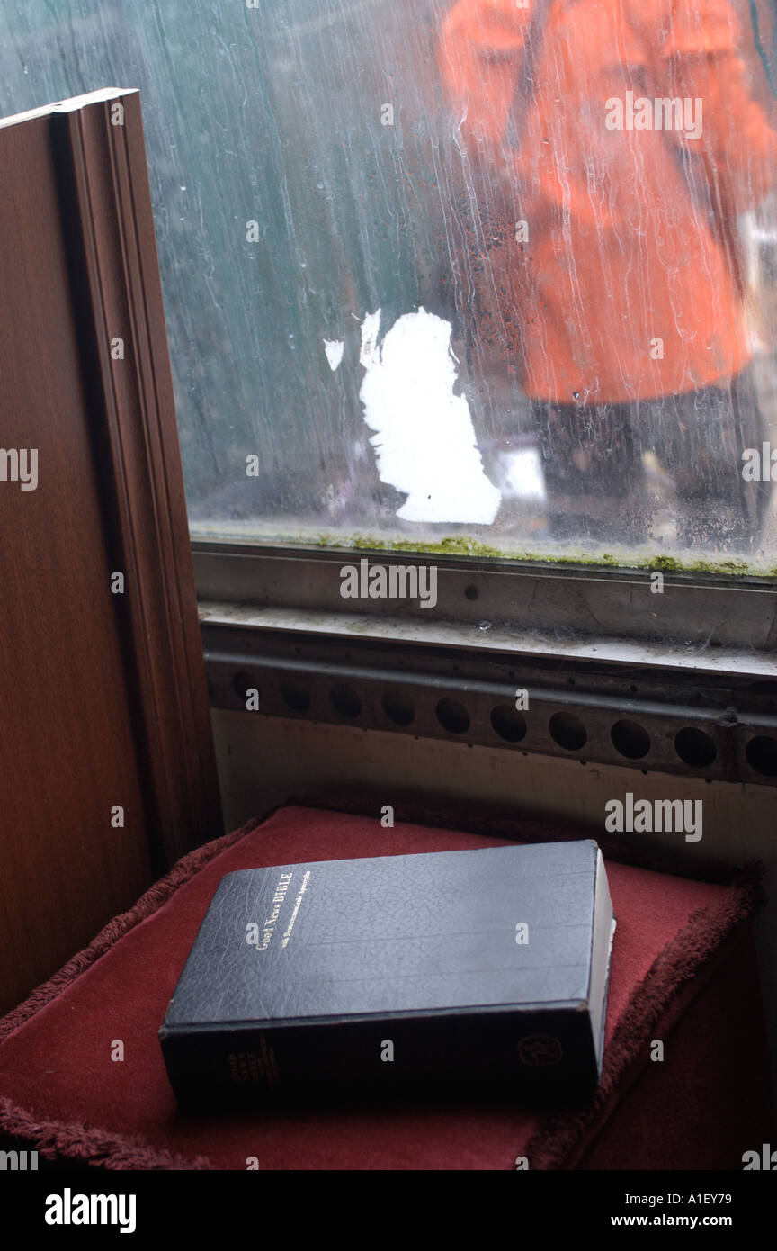 La Bibbia sul cuscino rosso a sinistra in un centro di riciclaggio a Dorset con uomo in giacca pioggia arancione visibile attraverso finestra Foto Stock