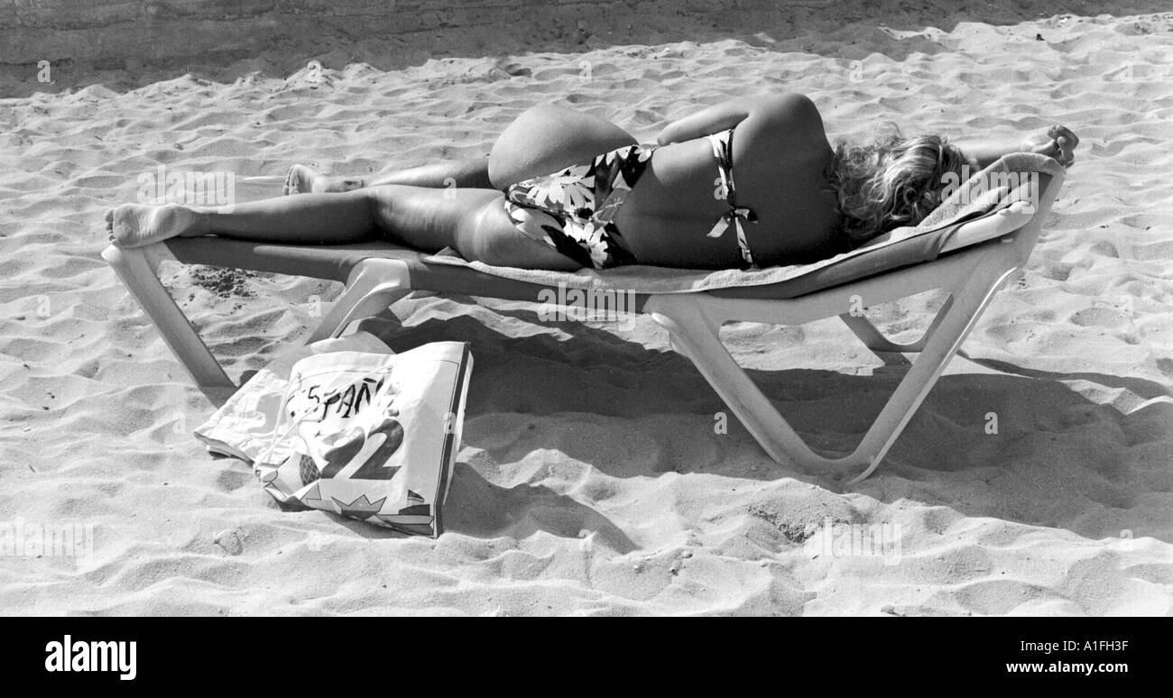 La donna posa sul sedile reclinabile in spiaggia a prendere il sole con torna alla fotocamera in Magalluf Maiorca Maiorca Foto Stock