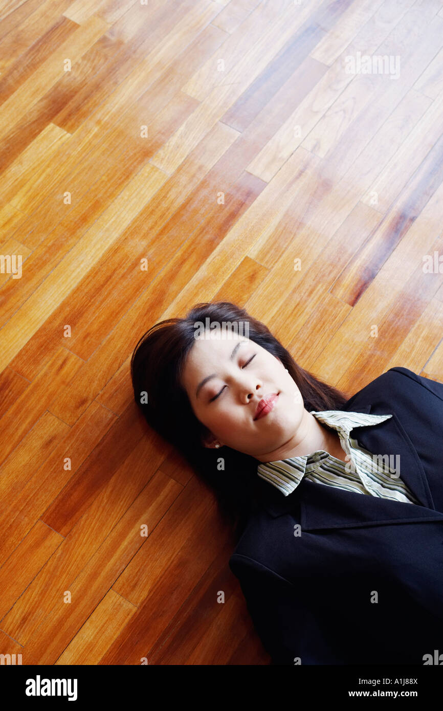 Angolo di alta vista di una imprenditrice sdraiato sul pavimento di legno con gli occhi chiusi Foto Stock