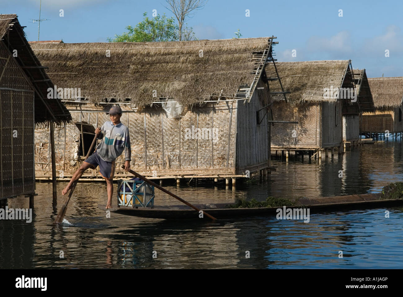 Alloggi su palafitte Inle Lake, Myanmar. Giovane canottaggio in modo tradizionale con la gamba. Gruppo di case del villaggio, tetti e pareti in rattan di legno. Foto Stock