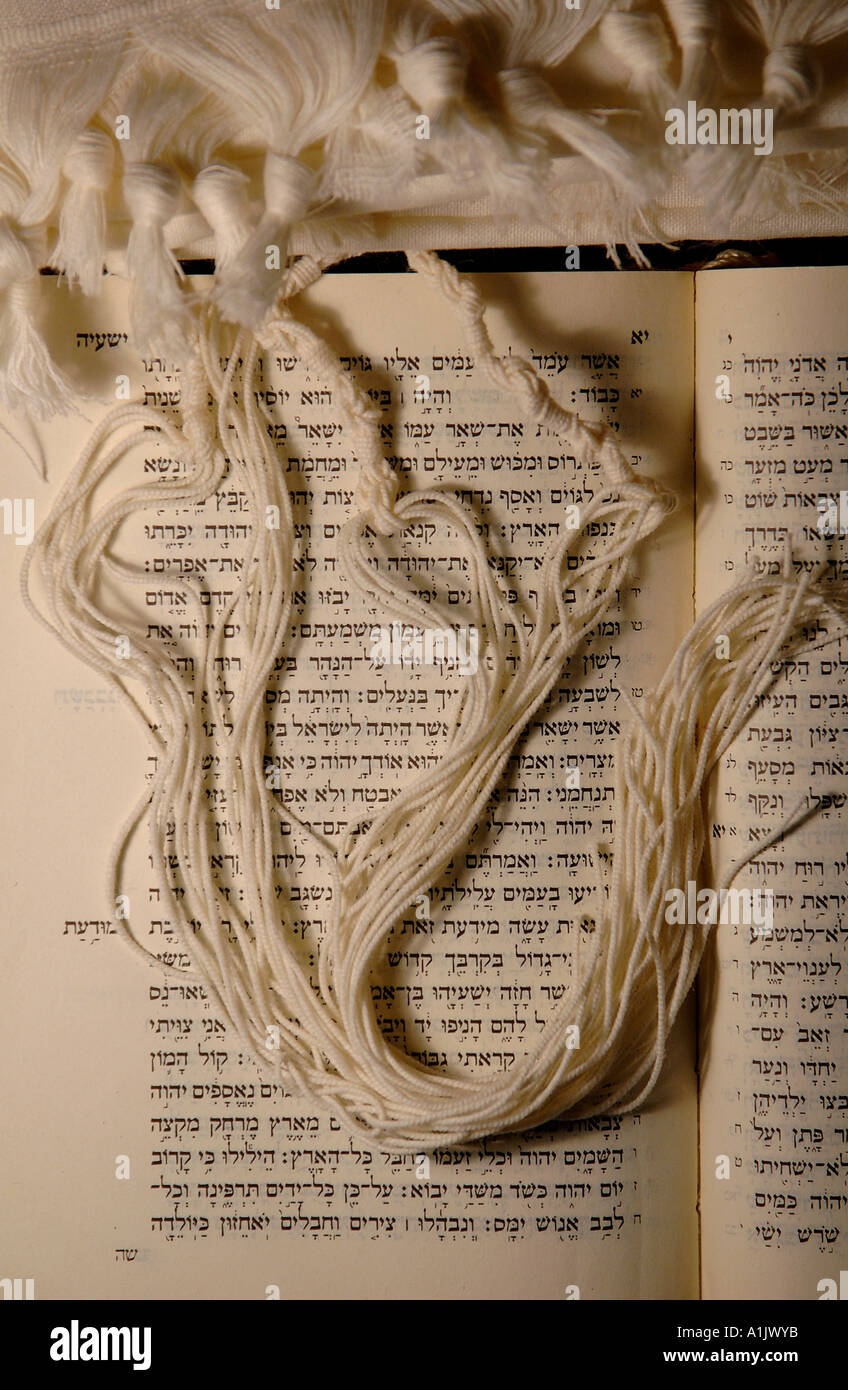 Tzitzis o tsitsiyot annodato frange rituali o nastole di un angolo di uno scialle di preghiera Talit indossato da ebrei osservanti che posano sulla bibbia ebraica Torah Foto Stock