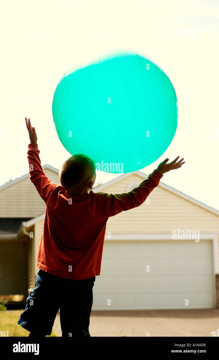 Ragazzo giovane gettando grande blu verde palla in aria Foto Stock