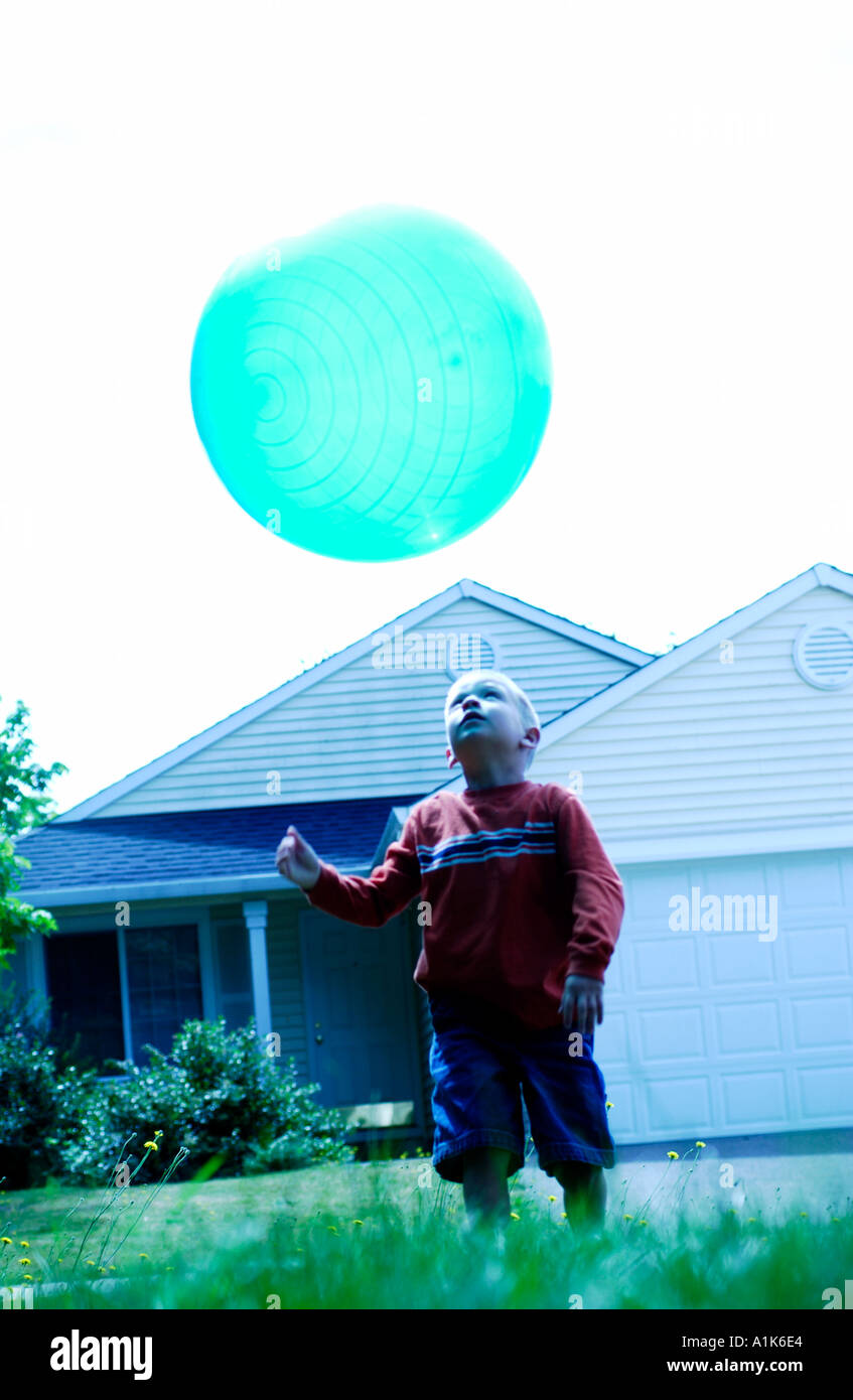 Ragazzo giovane gettando grande blu verde palla in aria Foto Stock